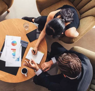 Due persone confrontano documenti di lavoro durante un incontro, per individuare le esigenze del cliente