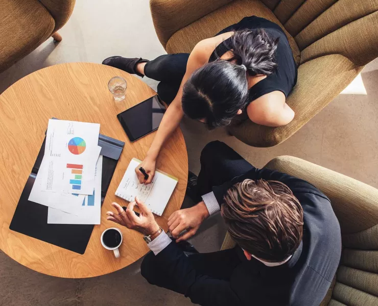 Due persone confrontano documenti di lavoro durante un incontro, per individuare le esigenze del cliente